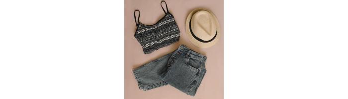 Geometric print crop top laid out with charcoal colored straight leg jeans and straw fedora hat with a black band