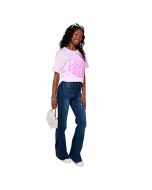 The female model wears a light pink Barbie palm tree tee, dark wash distressed hem denim flare jeans, and white sneakers while holding a white envelope clasp handbag with a gold chain handle.