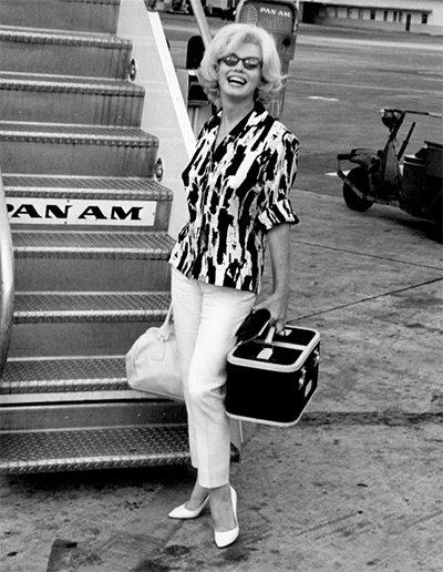 Marilyn Monroe in 1962 boarding a plane in a patterned silk print top, white ankle length pants and white pumps