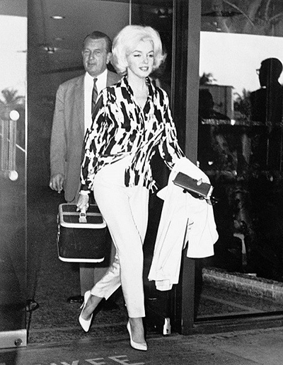 Marilyn Monroe in printed silk top, white ankle pants and white pumps exiting airport in 1962
