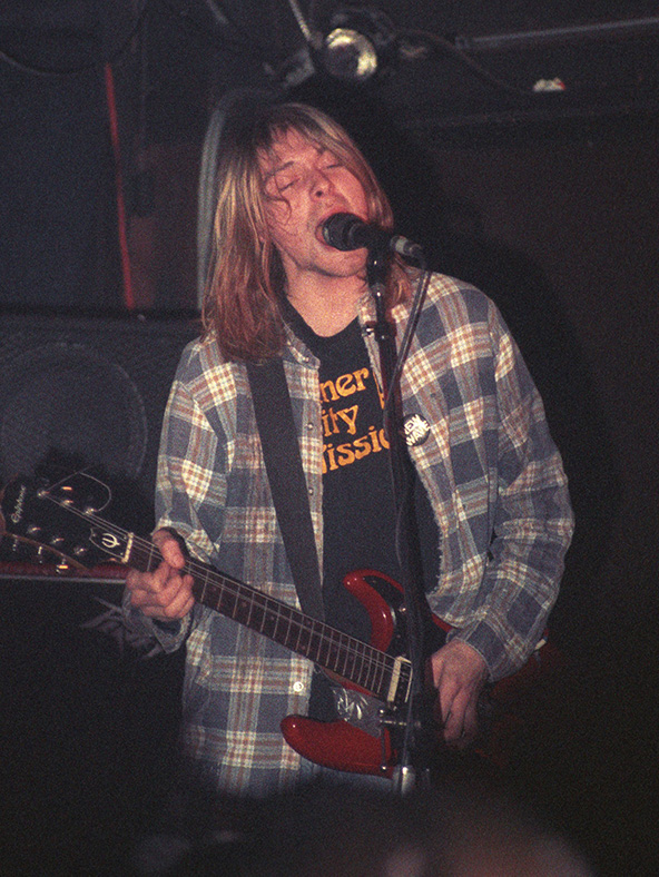 Pictured is the late lead singer of Nirvana, Kurt Cobain in a plaid flannel shirt while performing