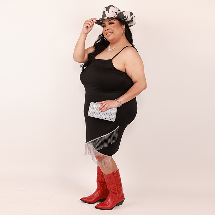 Plus size model wearing rhinestone fringe dress, cow print cowboy hat and red boots